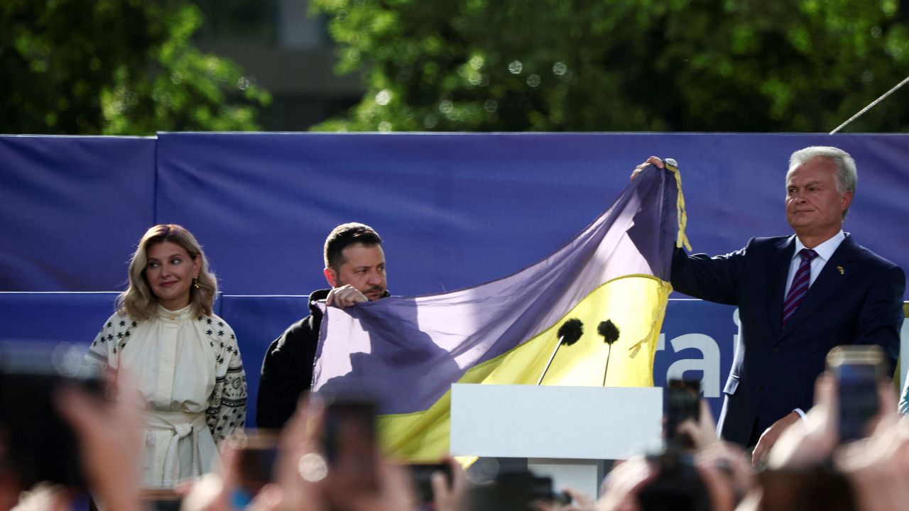 Ukrainian President Volodymyr Zelenskiy and Lithuanian President Gitanas Nauseda hold a Ukrainian flag from the frontline of the war with Russia, next to Olena Zelenska, during a ceremony, on the sidelines of a NATO leaders summit in Vilnius, Lithuania July 11, 2023. REUTERS/Kacper Pempel    